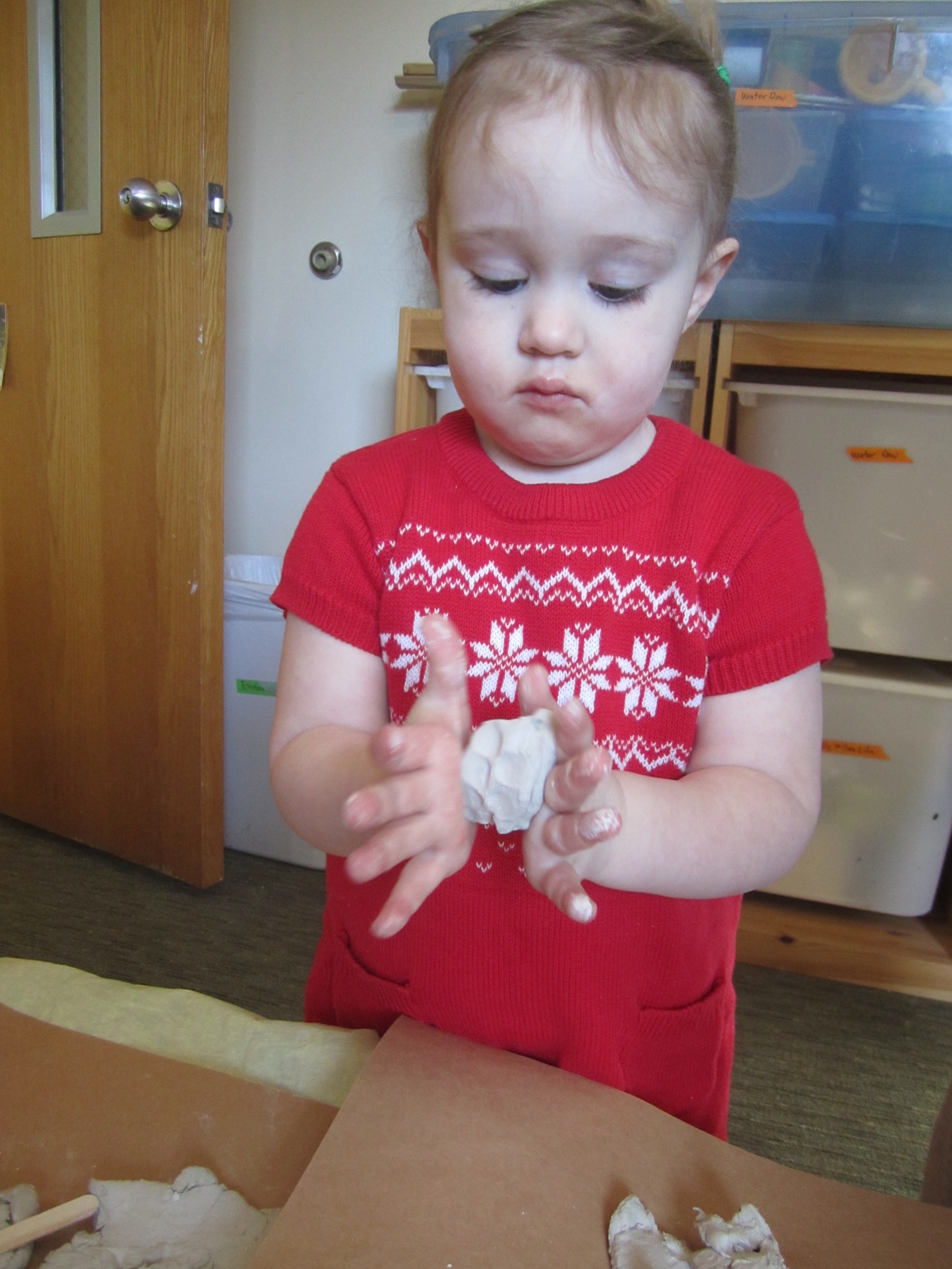 Child rolls clay between her hands.